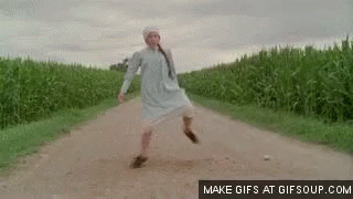 A Woman In A White Dress Is Walking Down A Dirt Road In A Field . GIF
