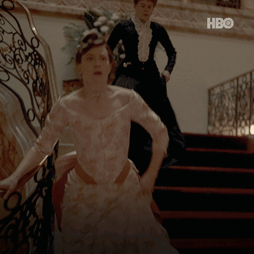 A Woman In A White Dress Is Walking Down A Set Of Stairs Next To A Woman In A Black Dress GIF