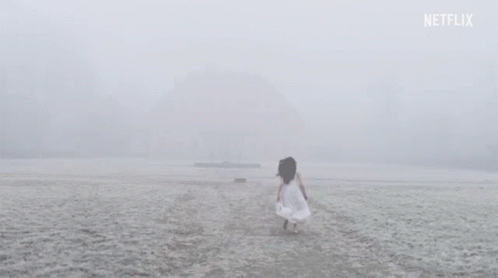 A Woman In A White Dress Is Walking On A Snowy Beach . GIF