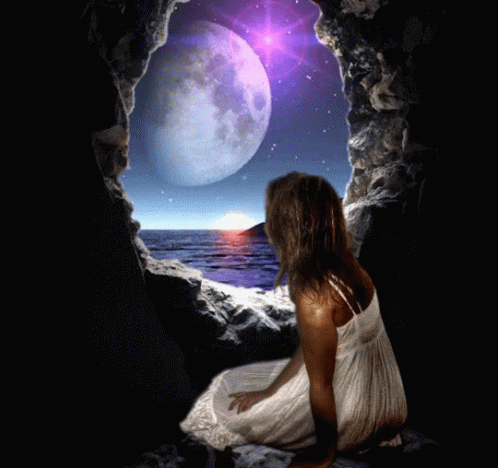 A Woman In A White Dress Sits In A Cave Looking At A Full Moon Over The Ocean GIF