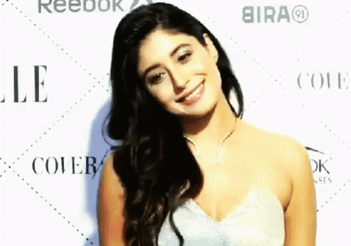 A Woman In A White Dress Smiles In Front Of Reebok And Bira GIF