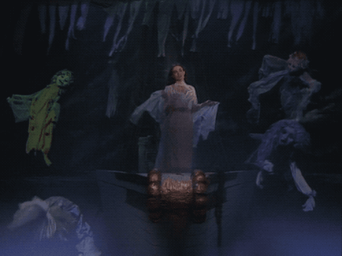 A Woman In A White Dress Stands In A Dark Room Surrounded By Ghosts GIF