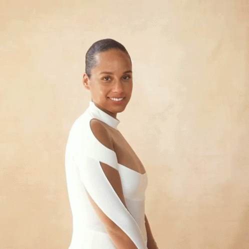 A Woman In A White Dress Stands In Front Of A Beige Background GIF