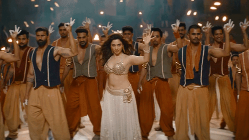A Woman In A White Dress Stands In Front Of A Group Of Men GIF