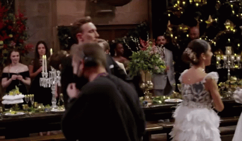 A Woman In A White Dress Stands In Front Of A Table With Candles On It GIF