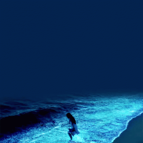 A Woman In A White Dress Stands In The Ocean GIF
