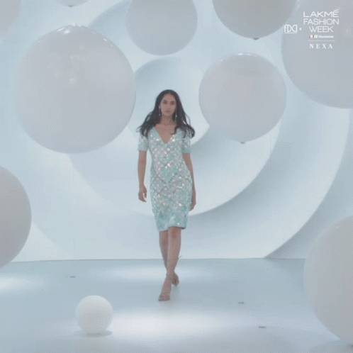 A Woman In A White Dress Walks Down A Runway At Lakme Fashion Week GIF