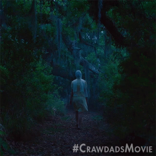a woman in a white dress walks through a dark forest