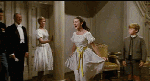 A Woman In A White Dress With A Yellow Belt Is Dancing In A Room GIF