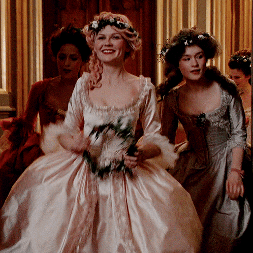 A Woman In A White Dress With Flowers In Her Hair Smiles GIF