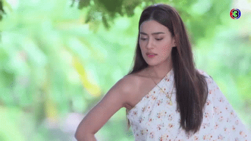 A Woman In A White Floral Dress Is Standing In Front Of A Tree . GIF