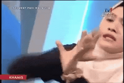 A Woman In A White Hijab Is Sitting In Front Of A Tv Screen That Says ' Selamat Pagi Malaysia ' On It GIF