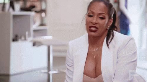 A Woman In A White Jacket And A Plunging Neckline Is Sitting On A Couch . GIF