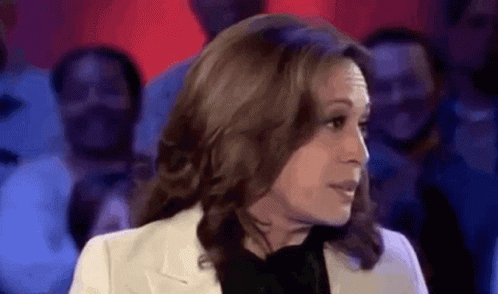 A Woman In A White Jacket And Black Shirt Is Talking To A Crowd Of People . GIF