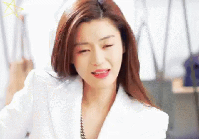 A Woman In A White Jacket And Red Lipstick Is Sitting In An Office . GIF