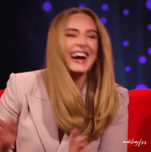 A Woman In A White Jacket Is Laughing While Sitting In A Chair GIF