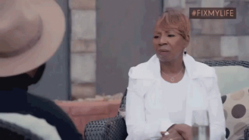 A Woman In A White Jacket Is Sitting In A Chair With A Glass Of Water . GIF