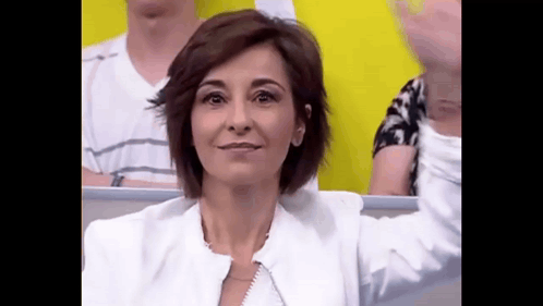 a woman in a white jacket is sitting in a stadium with her arms outstretched .