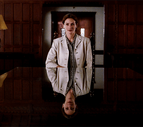 A Woman In A White Jacket Sits In A Chair With Her Head Down GIF