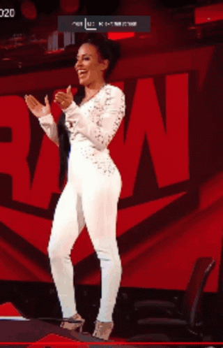 A Woman In A White Jumpsuit Is Clapping Her Hands In Front Of A Large Red N. GIF