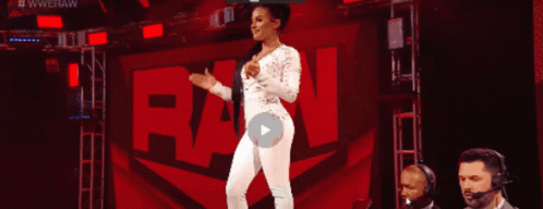 A Woman In A White Jumpsuit Is Standing In Front Of A Raw Sign GIF