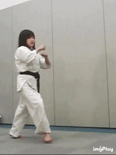 A Woman In A White Karate Uniform Is Kicking A Ball . GIF