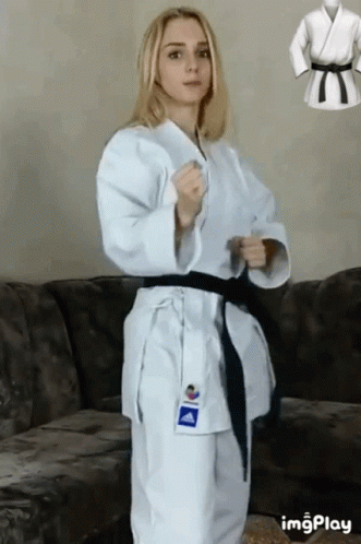 A Woman In A White Karate Uniform Is Standing Next To A Couch . GIF
