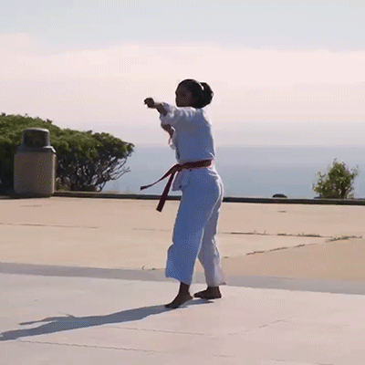 A Woman In A White Karate Uniform With A Red Belt Is Doing A Trick GIF