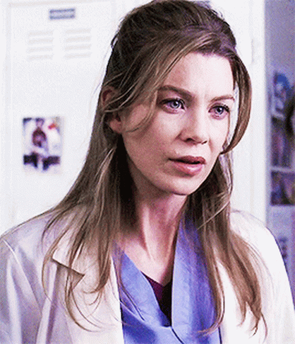 A Woman In A White Lab Coat And Blue Scrubs Stands In Front Of A Locker GIF