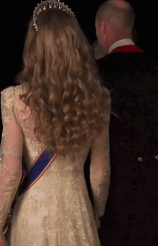 A Woman In A White Lace Dress With A Blue Sash Around Her Waist GIF