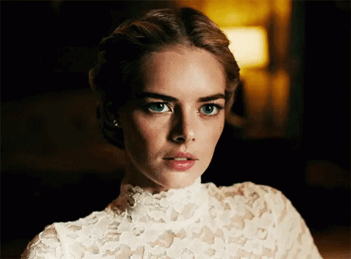 A Woman In A White Lace Top Is Looking At The Camera With A Serious Look On Her Face . GIF