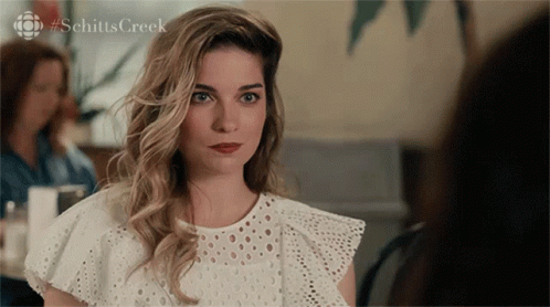 A Woman In A White Lace Top With #Schitts Creek On The Bottom GIF