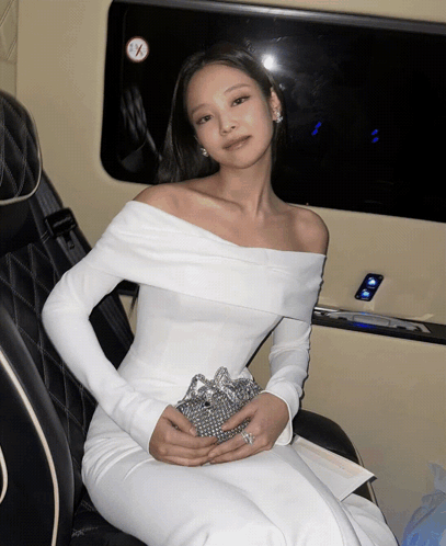 A Woman In A White Off The Shoulder Dress Is Sitting In A Car GIF