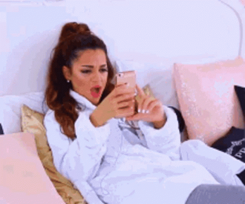 A Woman In A White Robe Is Laying On A Bed With Her Hands On Her Stomach . GIF