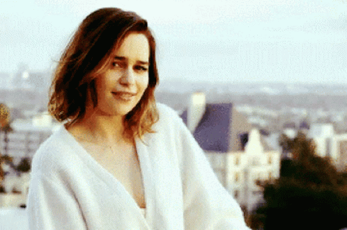 A Woman In A White Robe Is Smiling In Front Of A City GIF