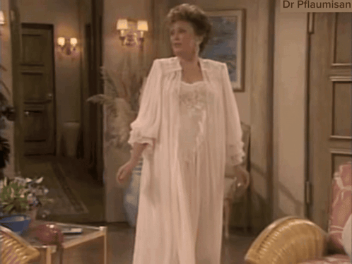 A Woman In A White Robe Is Standing In A Living Room With A Sign That Says Dr Pflaumisan GIF