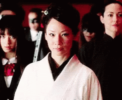 A Woman In A White Robe Is Standing In Front Of A Group Of People GIF