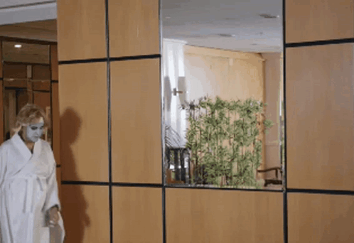 A Woman In A White Robe Is Standing In Front Of A Wooden Wall GIF