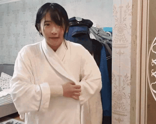 A Woman In A White Robe Stands In Front Of A Wall GIF