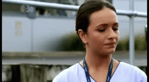 A Woman In A White Scrub Top With A Lanyard Around Her Neck Is Crying . GIF