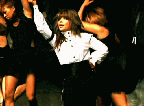 A Woman In A White Shirt And Black Pants Is Surrounded By Other Dancers GIF