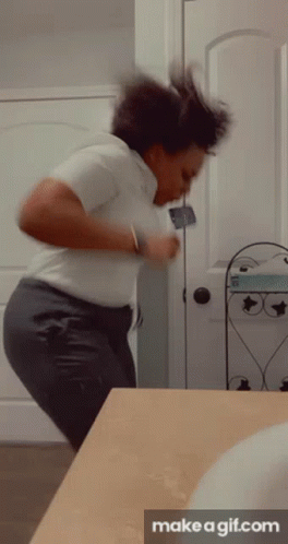 A Woman In A White Shirt And Gray Pants Is Dancing In Front Of A Bathroom Mirror . GIF
