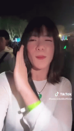 A Woman In A White Shirt And Green Wristband Is Standing In Front Of A Crowd . GIF