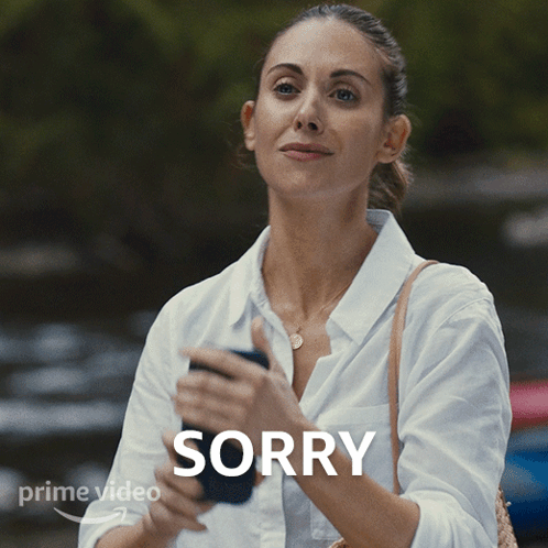 a woman in a white shirt is holding a cell phone with the word sorry above her