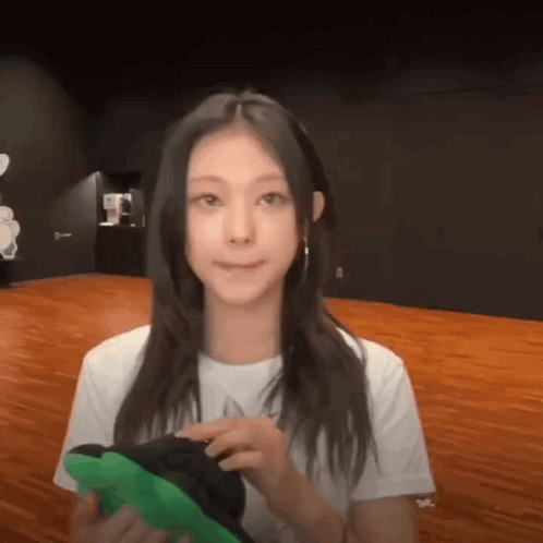 A Woman In A White Shirt Is Holding A Green Item In Her Hands GIF