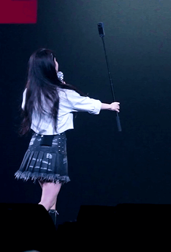 A Woman In A White Shirt Is Holding A Microphone In Her Hand GIF