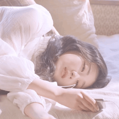 A Woman In A White Shirt Is Laying Down On A Bed GIF