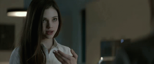 A Woman In A White Shirt Is Looking At A Man In A Dark Room . GIF