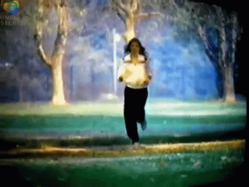 A Woman In A White Shirt Is Running In A Park With Trees In The Background .. GIF