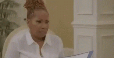 A Woman In A White Shirt Is Sitting At A Table Holding A Piece Of Paper In Her Hand . GIF